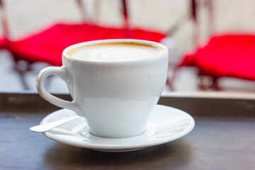 A white cup of cappuccino coffee on saucer on table on cafe, restaurant terrace.