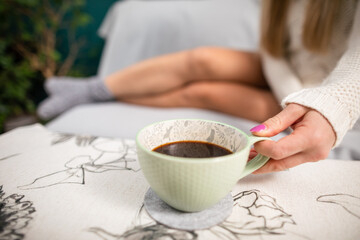 The slim legs of a sexy girl. She is holding a cup of hot coffee.