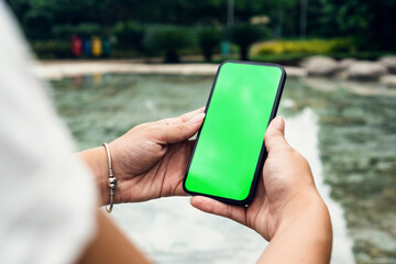 Girl in the park holding a smartphone with Green screen. Wooden bridge, green area and an...