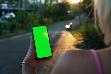 Girl on the street holding a smartphone with Green screen. Sunset. Tress around. Chroma Key