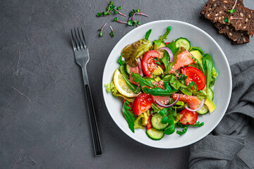Salad with salmon, avocado, cucumber and tomatoes on a graphite background.