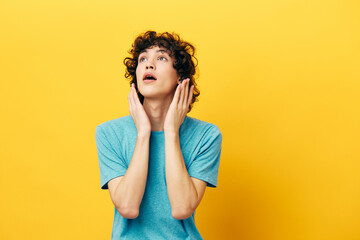 guy with curly hair holds his hands near his face yellow background