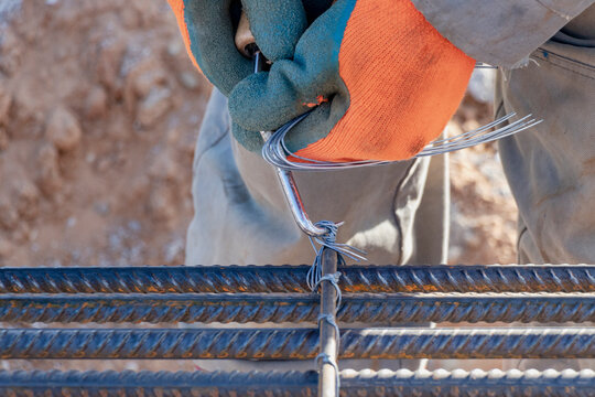 A worker uses steel tying wire to fasten steel rods to reinforcement bars. Close-up. Reinforced concrete structures - knitting of a metal reinforcing cage.