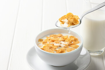 Corn flakes with fresh milk on white wooden table.