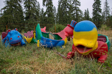 Abandoned colorful attraction animal shaped boats left in untrimmed grass after rain in summer 