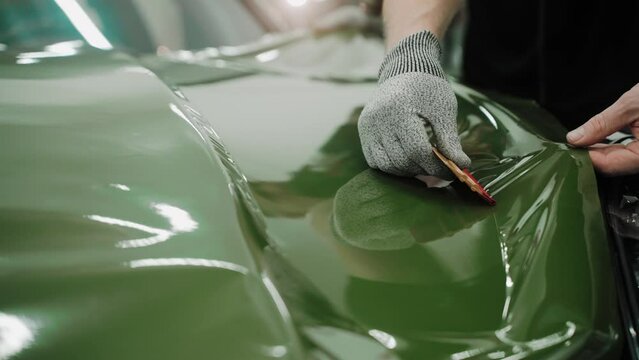 Process of vinyl wrapping a car hood in dark green color using plastic cards. Process of vinyl wrapping a car hood in a car studio. Shiny khaki green car vinyl wrap. High quality 4k footage