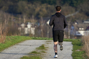 Mann in kurzer Hose und Kapuzenjacke joggt auf einem Feldweg
