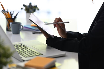 Cropped image of creative designer holding stylus pen and writing on digital tablet.