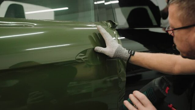 Close up shot of man vinyl wrapping the car door, smoothing the film with fingers. Process of vinyl wrapping a car in a garage. Smoothing vinyl film for car wrapping. High quality 4k footage