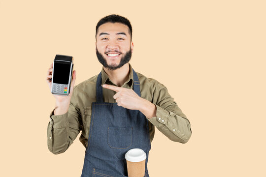asian waiter with coffee, holding dataphone paying with credit card on beige background