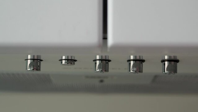 A finger presses a metal button on a kitchen hood to turn it on and off. Ventilation in the house above the hob. White household appliances