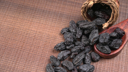 black raisins in a bowl on a wooden table. black raisins in a spoon