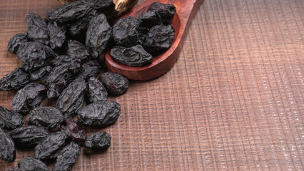 black raisins in a bowl on a wooden table. black raisins in a spoon