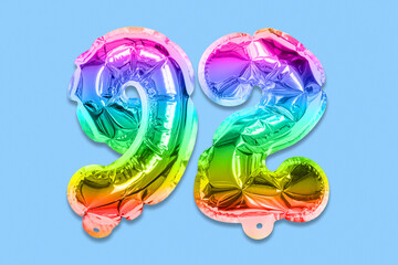 Rainbow foil balloon number, digit ninety two on a blue background. Birthday greeting card with inscription 92. Top view. Numerical digit. Celebration event, template.