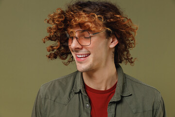 Close up fun fancy vivid young brunet curly man 20s wears khaki shirt jacket glasses waving fooling around have fun enjoy play fluttering hair isolated on plain olive green background studio portrait.