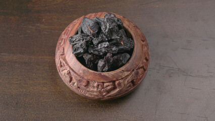 black raisins in a bowl on a wooden table. black raisins in a spoon