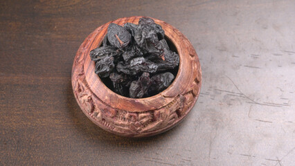black raisins in a bowl on a wooden table. black raisins in a spoon