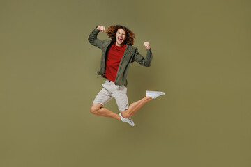 Full size body jubilant overjoyed exultant young brunet curly man 20s wears khaki shirt doing winner gesture celebrate clenching fists jumping isolated on plain olive green background studio portrait.