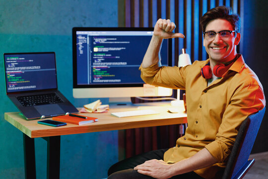 Young satisfied confident professional software database engineer IT programmer man in shirt work at home writing code on laptop pc computer point thumb finger on himself. Program development concept.