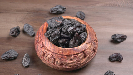 black raisins in a bowl on a wooden table. black raisins in a spoon