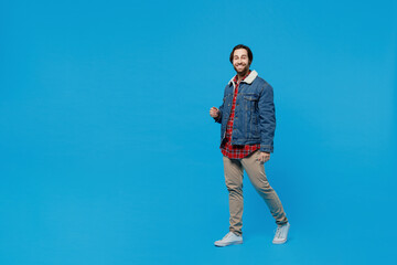 Full size body length happy young brunet bearded man 20s wears warm denim jacket go move look camera smiling isolated on plain pastel light blue background studio portrait. Winter cold season concept.