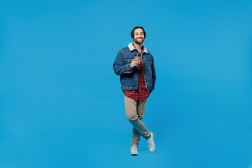 Obraz premium Full size young brunet bearded man 20s in denim jacket hold takeaway delivery craft paper brown cup coffee isolated plain pastel light blue background studio portrait. Winter cold season concept