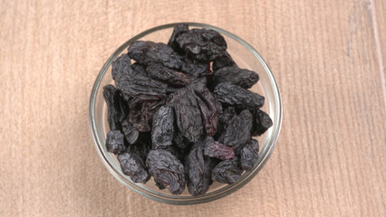 black raisins in a bowl on a wooden table. black raisins in a spoon