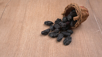 black raisins in a bowl on a wooden table. black raisins in a spoon