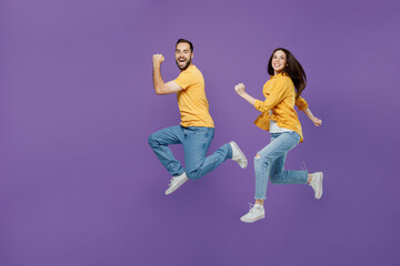 Full size young excited cheerful fun overjoyed couple two friends family man woman together in yellow casual clothes jump high run fast hurry up isolated on plain violet background studio portrait