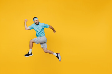 Fototapeta na wymiar Full body side view strong young fitness trainer instructor sporty man sportsman wear headband blue t-shirt jump high run fast look aside isolated on plain yellow background. Workout sport concept