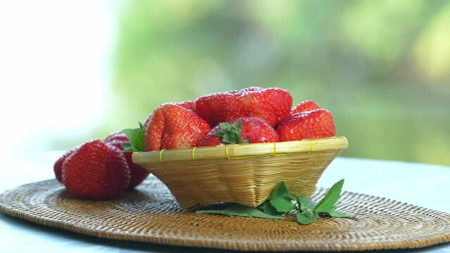 Red strawberry in Bamboo basket on wooden table, Fresh Red strawberries with leaves over green natural Blur background.