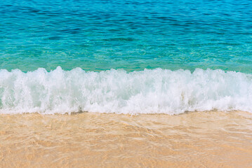 Summer scene with blue sea water, white foam and yellow sand close up with selective focus. Vacation or holiday concept. Nature background with copy space