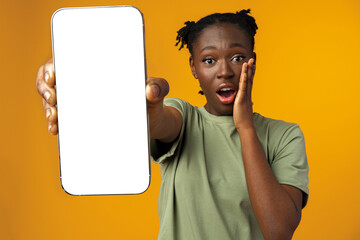 Young smiling african american woman showing smartphone with blank screen against yellow background