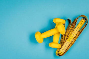 Yellow dumbbells and measuring tape on a blue background with a place to copy.