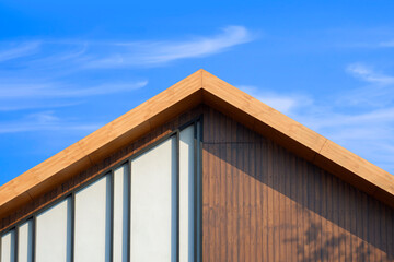 Sunlight on surface of vintage wooden gable roof with battens decoration against cloud on blue sky...