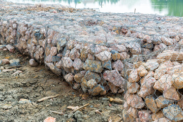 Stone walls, protection from backshore erosion. Stones in a metal mesh. Gabion wall constructed using steel wire mesh basket. Steel gabion filled with granite rocks at river bank.