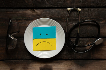 The flag of Ukraine is yellow and blue on paper and a painted sad smile in a plate on the table....