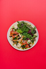 Italian Piadina with prosciutto, sun-dried tomatoes, greens mix, pesto, bechamel and mozzarella. Red background. top view