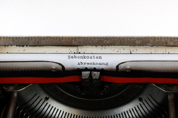 The German word Nebenkosten Abrechnung  written in red on an old mechanical typewriter Deuscher Text: Service charges billing