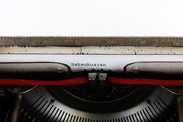 The German word Nebenkosten written in red on an old mechanical typewriter Deuscher Text: Service charges
