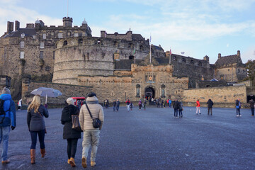 View of the medieval Edinburgh castle front gate with crowd of people walking in morning with clouds in clear blue sky background.