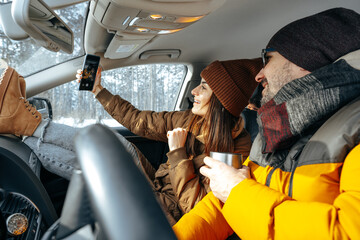 Family couple sitting in car in winter clothes iin snow forest