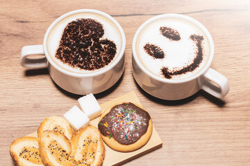 Top view image of two cups of coffee and hot chocolate with heart and smile on wooden table background.
