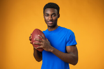 Young african player man playing rugby holding american football ball over yellow background