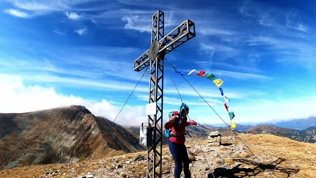 Woman and summit cross of mount Seckauer Zinken in the Seckau Tauern in Styria, Austria. Nepalese or Tibetan prayer flags are attached to it and strong wind is blowing. Freedom in the Austrian Alps

