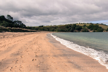 Coastline with sand beach, blue sea and green hill on background, Te Haruhi Bay, New Zealand.
