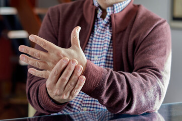 Middle-aged man sitting at home with pain in his hands due to osteoarthritis or rheumatism.