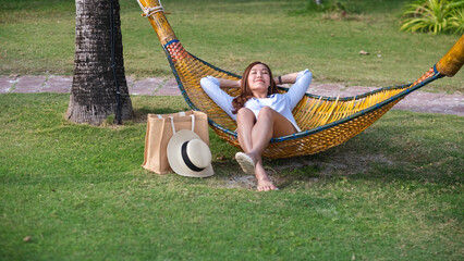 Portrait image of a beautiful young asian woman with hat laying down on bamboo hammock in a...