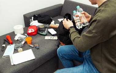Young man packing the bag with documents, water,food, first aid kit and other items needed to...