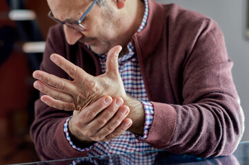 A middle-aged man is wincing and his left hand hurts because he has arthritis, rheumatism,...